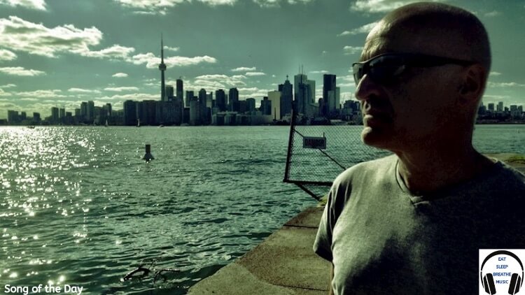 Singer Chris Birkett In front of the water with a city behind it