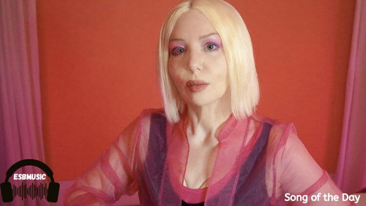 Multi-instrumentalist Jenn Vix in a pink shirt against a red background | "Mr Strange" Song of the Day Feature | Eat Sleep Breathe Music